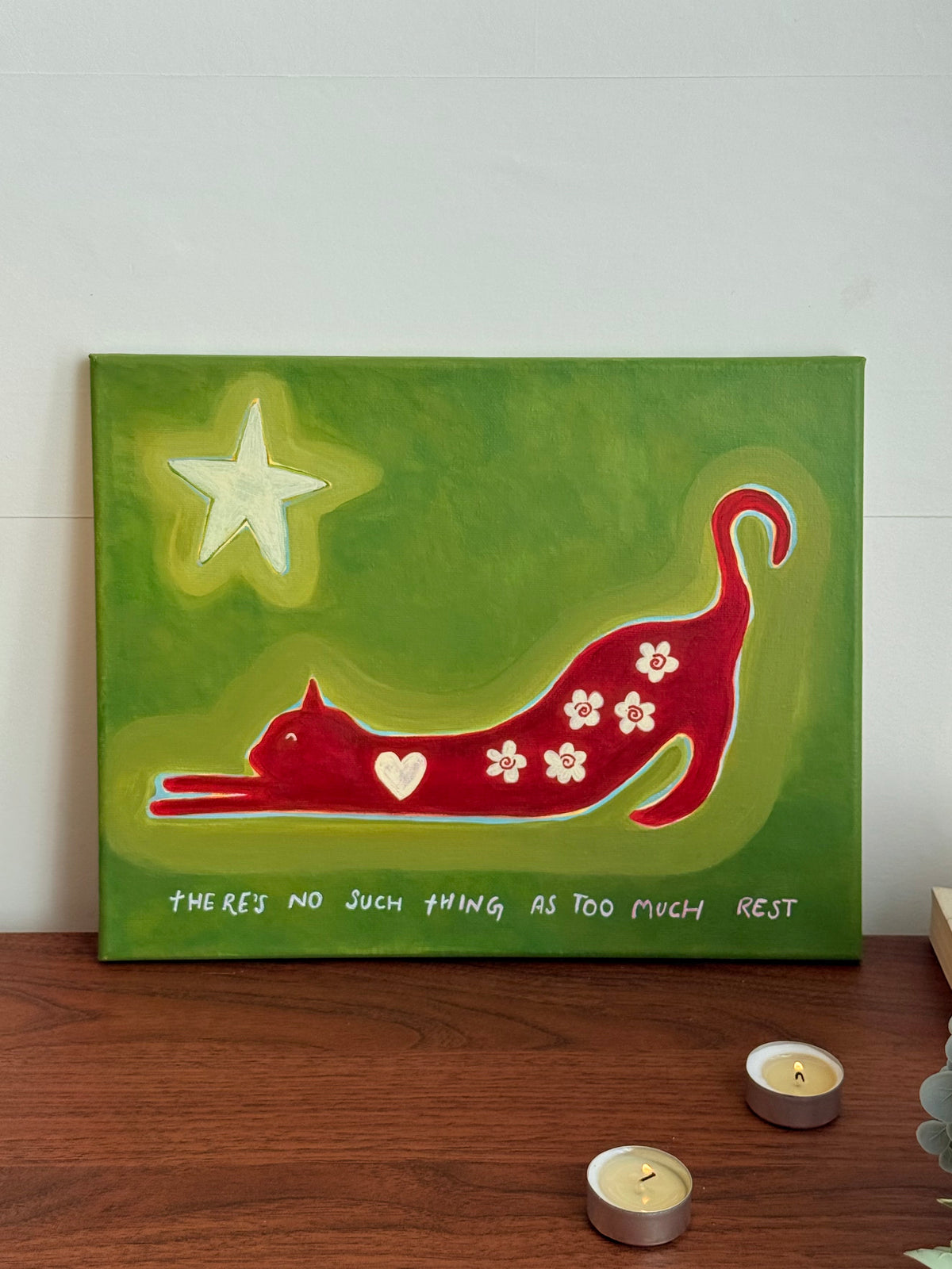 Original cat canvas styled beside a table lamp, books and a trailing plant