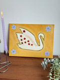 Swan painting on wooden shelf with gold pot plant and lavender candle — close crop